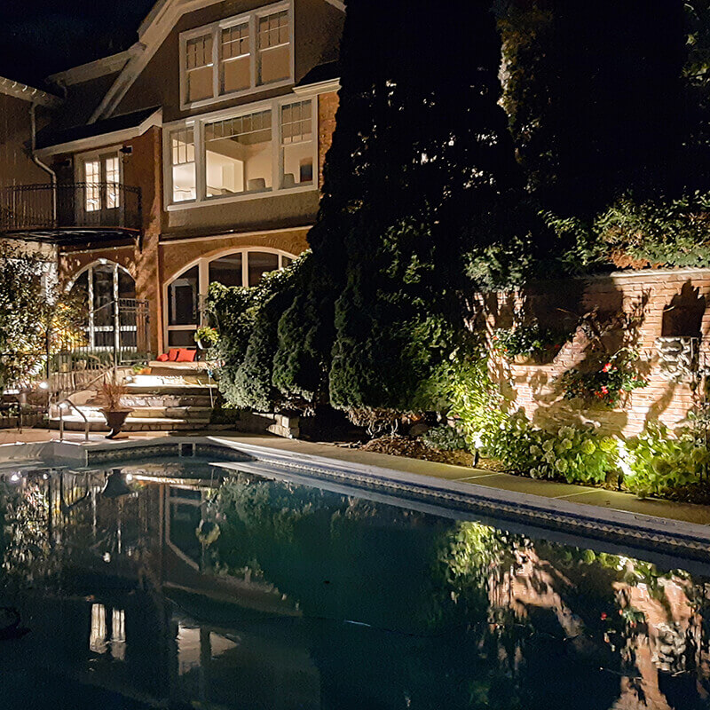 Pool with lighting around and a house in the background